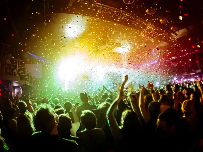 Shiny rainbow confetti during the concert and the crowd of people silhouettes with their hands up.