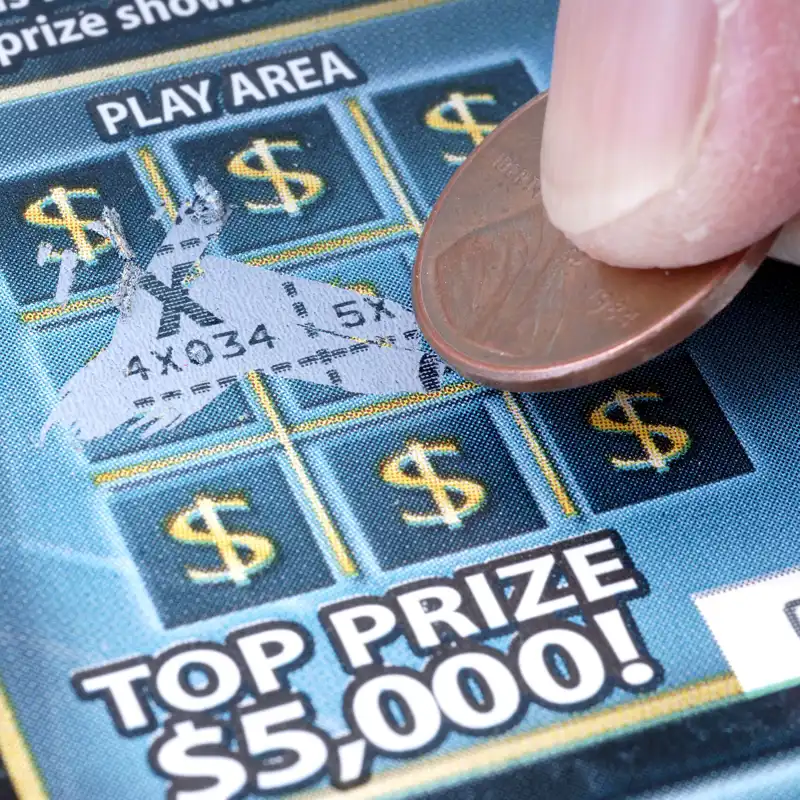 Closeup of a hand scratching a lottery ticket with a penny.