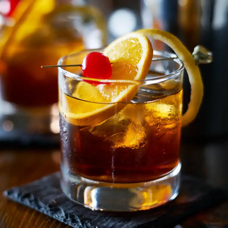 Tasty alcoholic old-fashioned cocktail with orange slice, cherry, and lemon peel garnish.