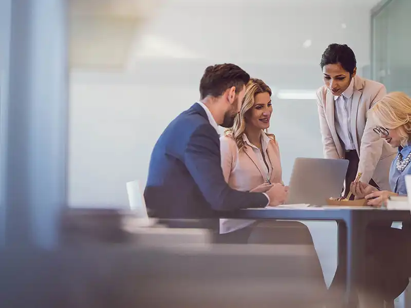 Four professionals looking at a laptop, while at a desk.