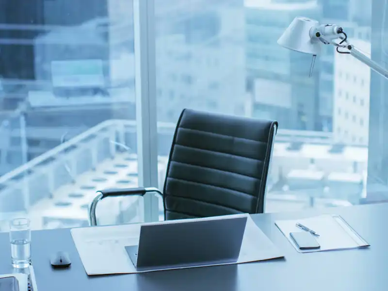 Laptop on a desk with a black leather chair.