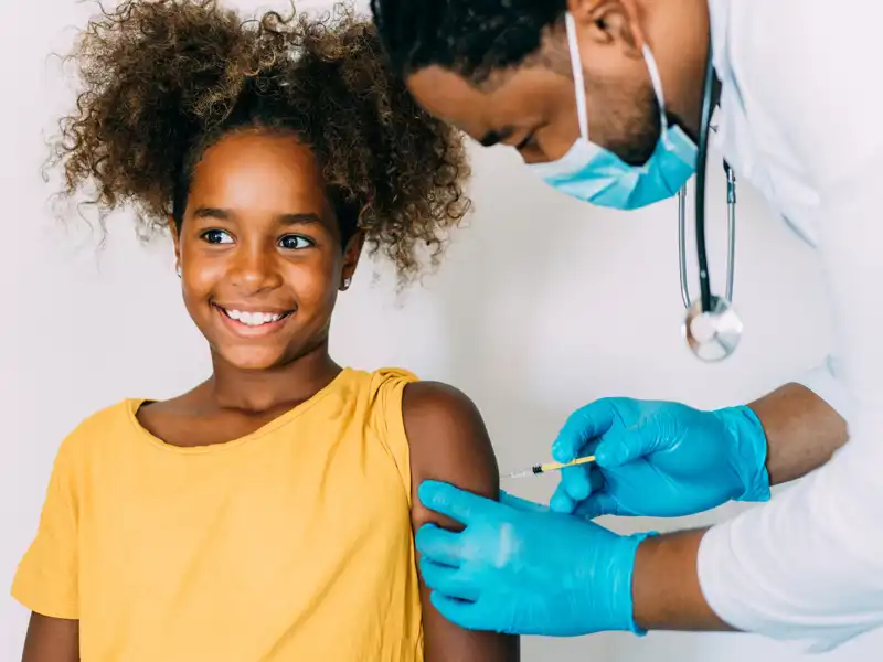 A girl is smiling as she gets vaccinated by a doctor.