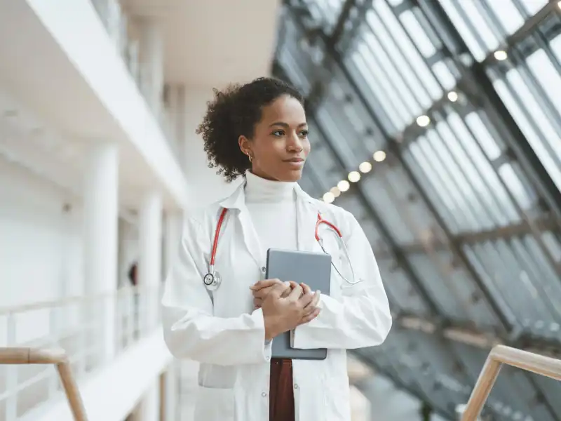A physician looks out the windows of a long hallway