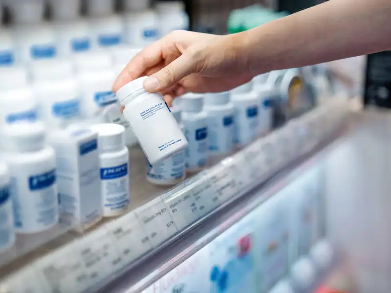 A person holding a medicine container in front of a shelf stocked with various medications.