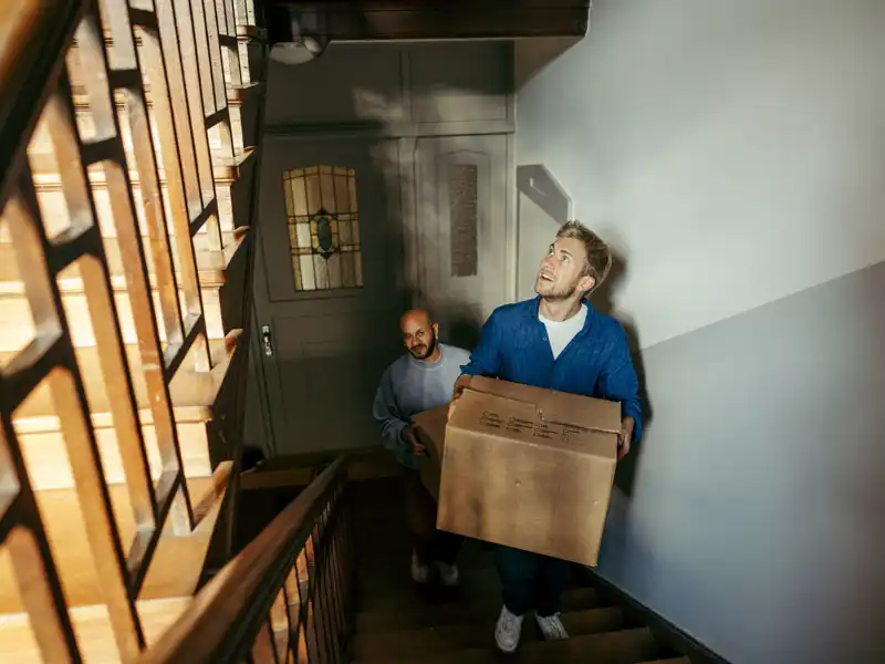 Two men carrying moving boxes up the stairs.