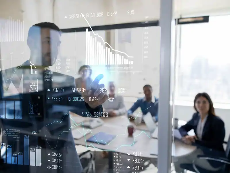 A man points out figures on a chart to professionals a meeting room