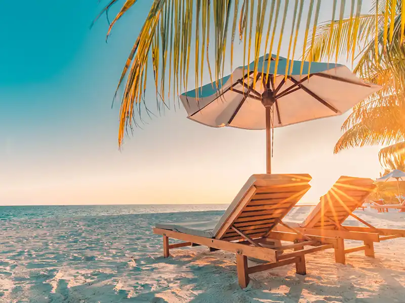 Two wooden slat reclining chairs and an umbrella on a sunny beach