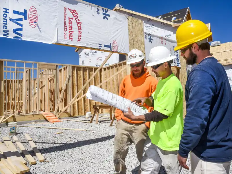 Three male construction workers, carpenters, wearing hardhats looking at blueprints.