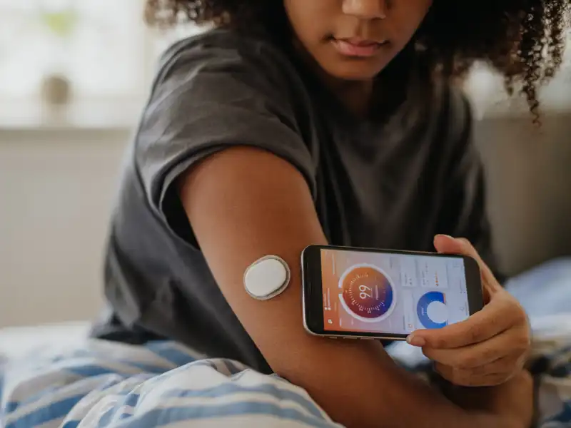 A woman sitting in bed, engaged with her smartphone, testing her blood sugar.